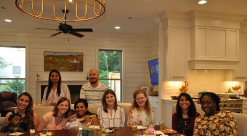 Students gather around a large table for a meal in a home.